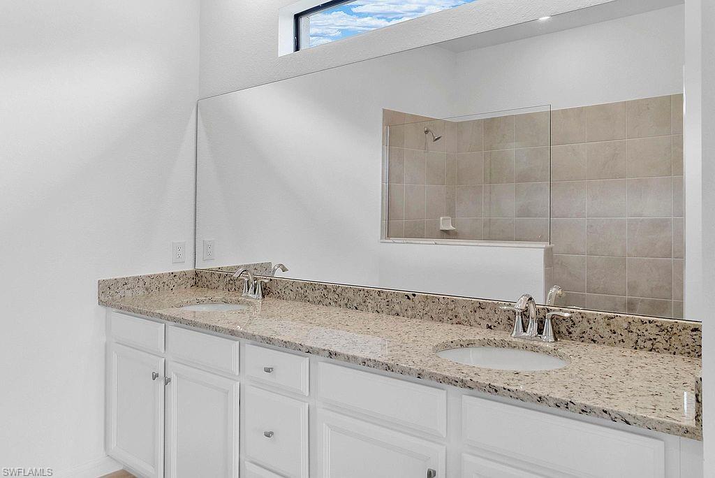 Spacious bath featuring a double vanity with stone countertops, integrated sinks, and chrome fixtures