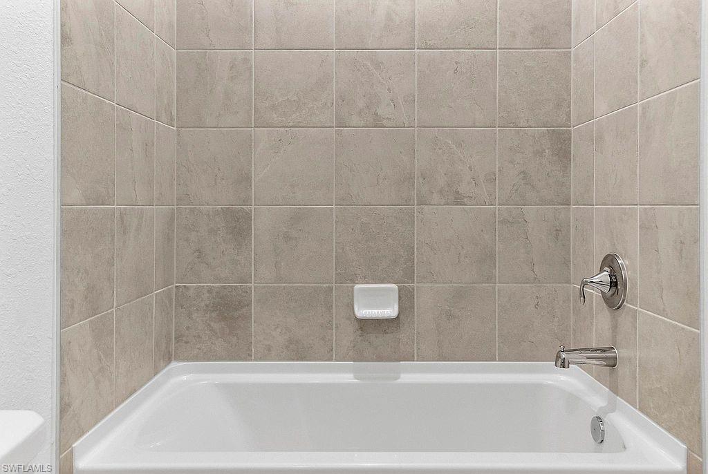 White soaking tub featuring polished chrome fixtures, integrated soap dish, and neutral-toned wall tiling