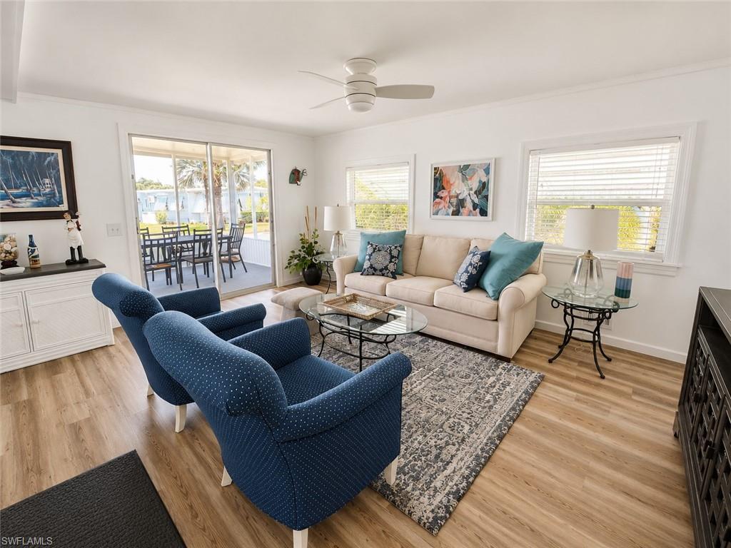 Bright and airy living space showcasing hardwood flooring throughout, abundant natural light from multiple large windows, a ceiling fan with integrated lighting, and built-in cabinetry with display shelving