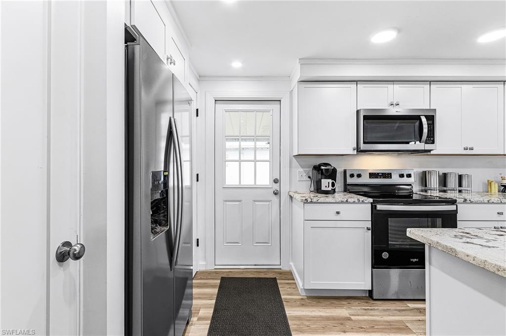 Modern kitchen featuring white shaker cabinetry, stainless steel appliances, granite countertops, wood-finish flooring, and recessed lighting