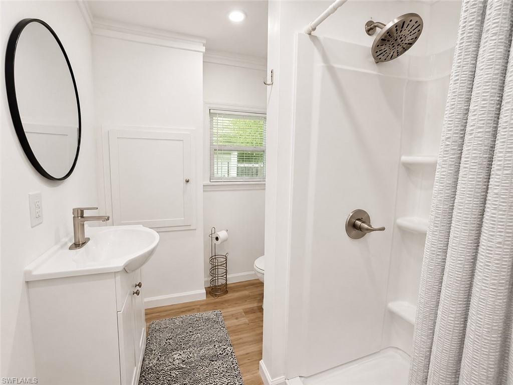 White single-sink vanity with brushed nickel faucet, wood-finish flooring, and a white shower stall with built-in shelving