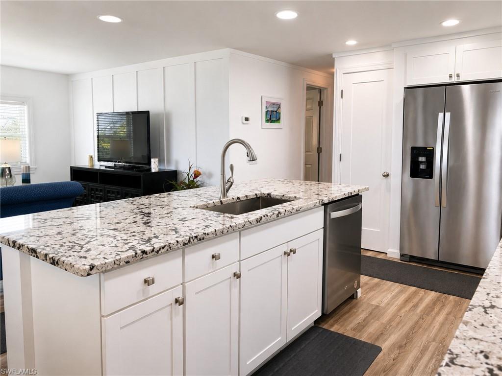 Contemporary kitchen featuring a large island with speckled stone countertops, white cabinetry with brushed nickel hardware, and stainless steel appliances including a dishwasher and refrigerator with ice/water dispenser