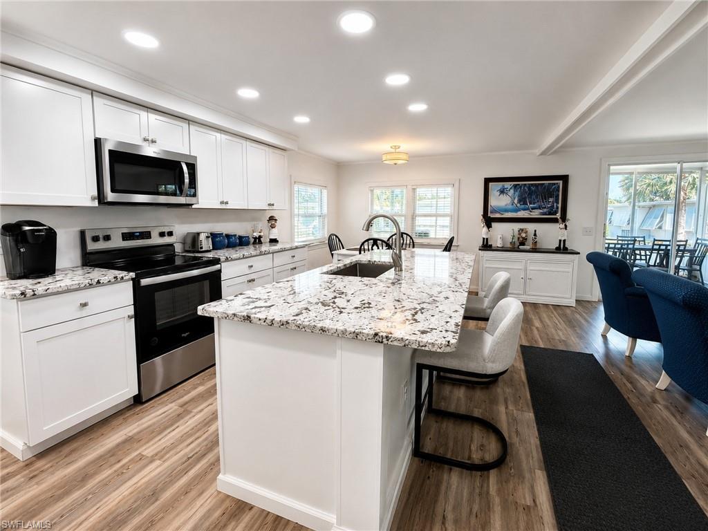 Spacious kitchen featuring an expansive central island with a sink, white cabinetry, granite countertops, and stainless steel appliances