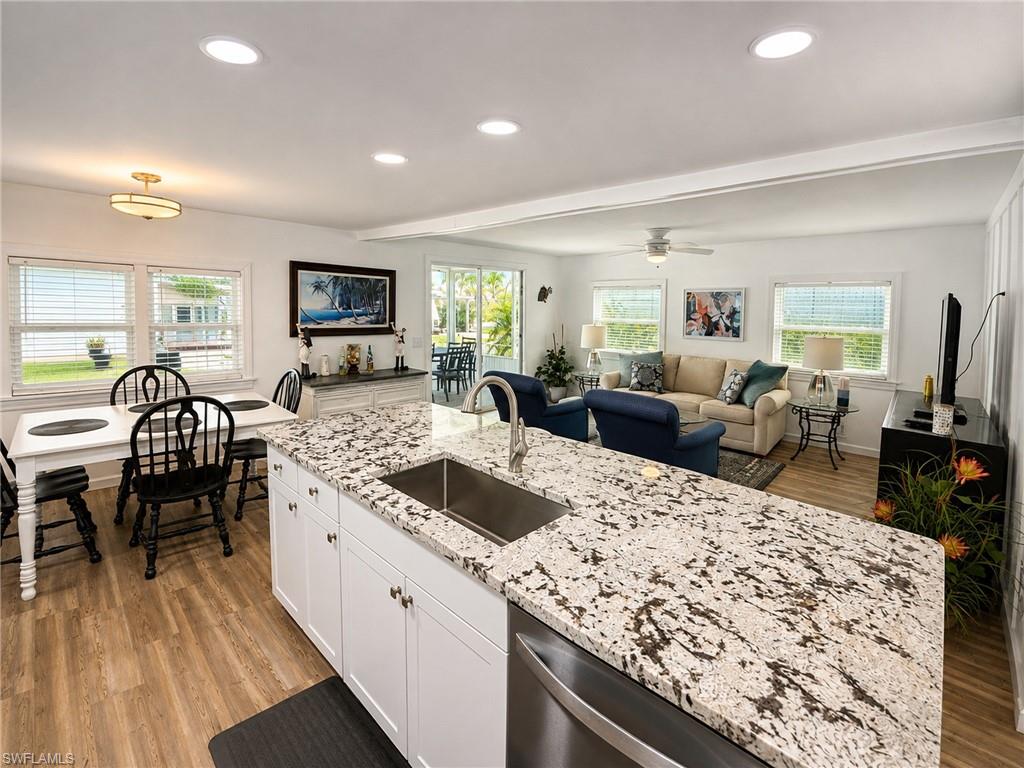 Open-concept living area featuring wood-finish flooring, recessed lighting, a kitchen island with stone countertop, and white cabinetry