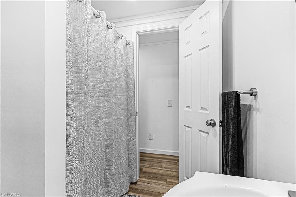 Bathroom featuring wood-finish flooring, a white paneled door, and a shower with a curved curtain rod
