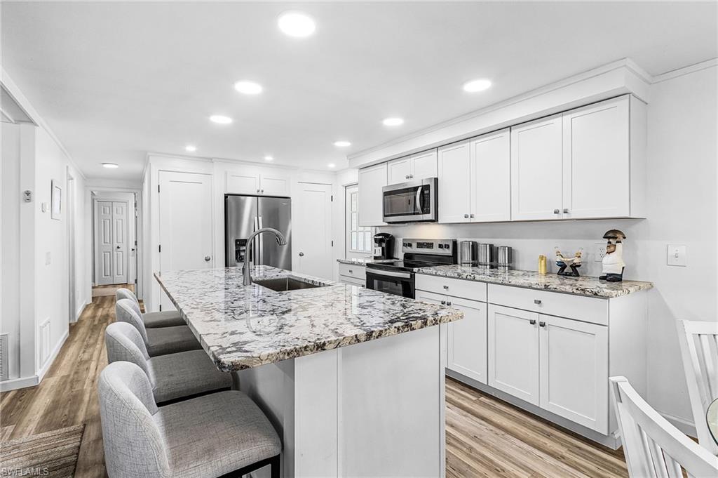 Contemporary kitchen featuring an oversized island with an undermount sink, stainless steel appliances, white cabinetry, and recessed lighting