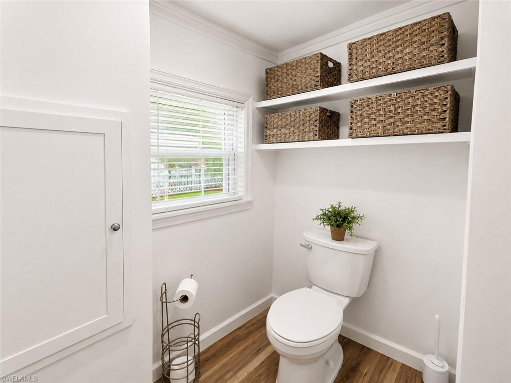 White toilet with dual flush, wood-finish flooring, and built-in shelving
