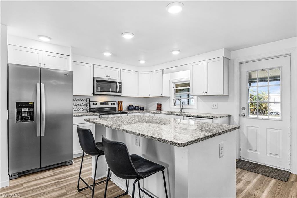 Expansive kitchen island with a stone countertop, wood-finish flooring, and pendant lighting