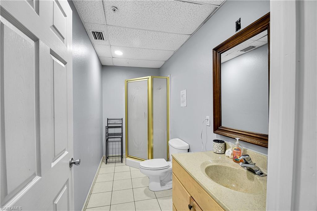 Bathroom featuring a wood-finish vanity with an integrated sink, a framed mirror, and a corner shower with a gold-finish frame