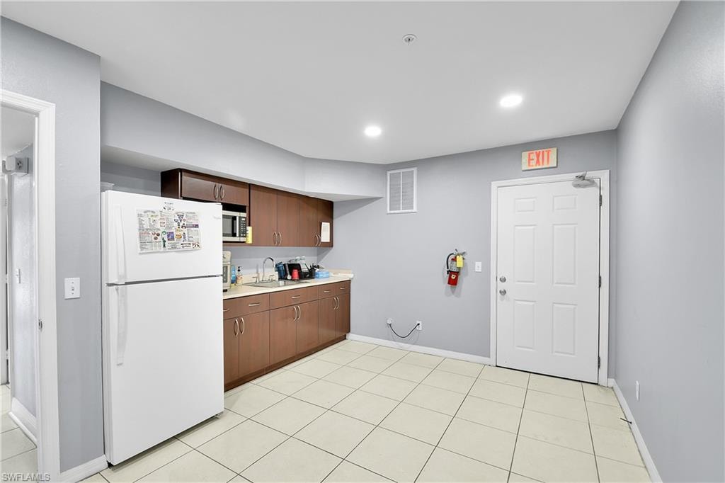 Kitchenette featuring wood-finish cabinetry, a stainless steel sink, and light-toned tile flooring