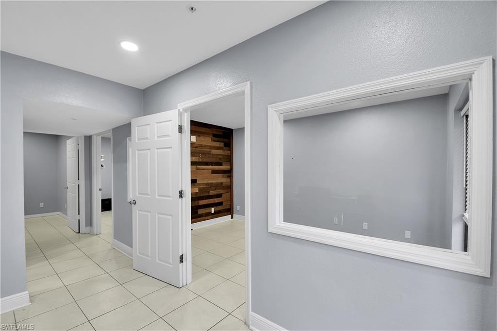 Interior hallway featuring light-colored tile flooring, multiple paneled doors, and recessed lighting