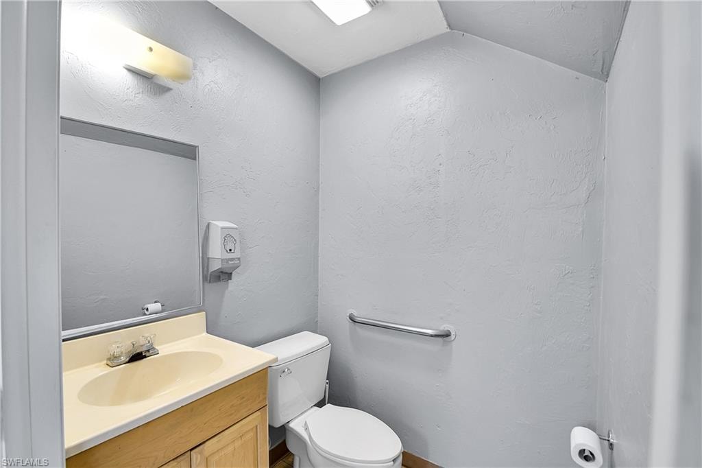 Bathroom featuring a vanity with an integrated sink, a wall-mounted mirror, a standard toilet, and a grab bar