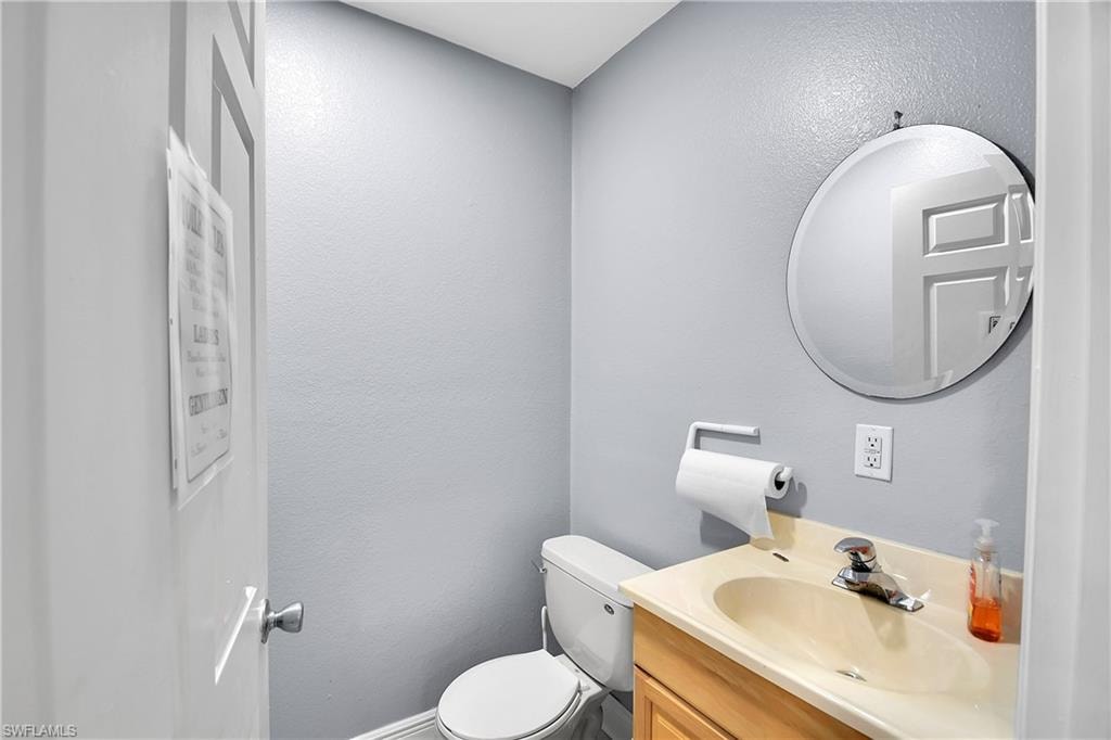 Powder room featuring a toilet, built-in vanity with integrated sink, chrome faucet, and a round wall-mounted mirror