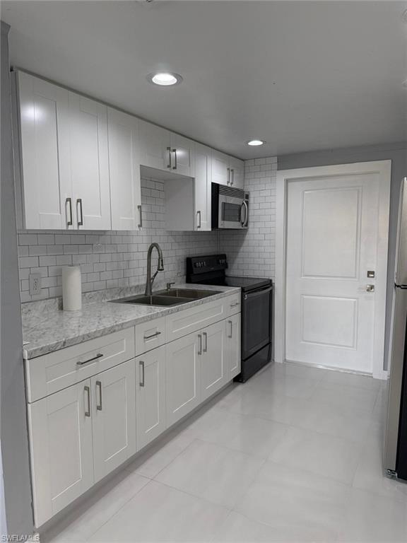 Contemporary kitchen featuring white shaker cabinetry, light-toned countertops, subway tile backsplash, stainless steel appliances, and recessed lighting