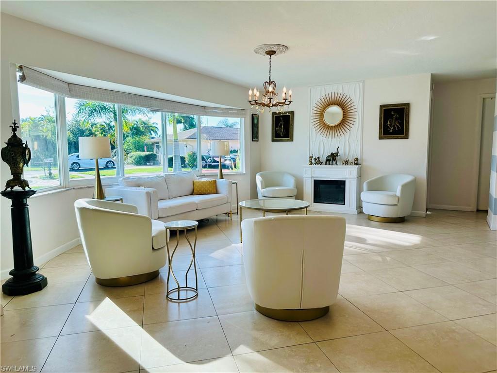 Spacious living area featuring large bay windows, a decorative fireplace with an ornate surround, tile flooring, and a chandelier with a ceiling medallion
