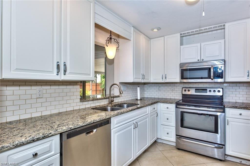 Kitchen featuring white shaker-style cabinetry, a subway tile backsplash, granite countertops, and stainless steel appliances including a double-basin sink with a gooseneck faucet