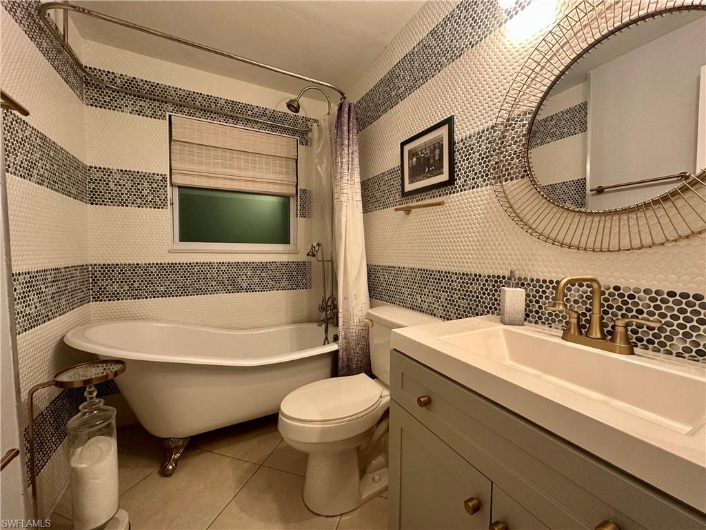 Bathroom featuring a freestanding clawfoot tub, mosaic tile accent walls, a vanity with integrated sink, and an ornate circular mirror