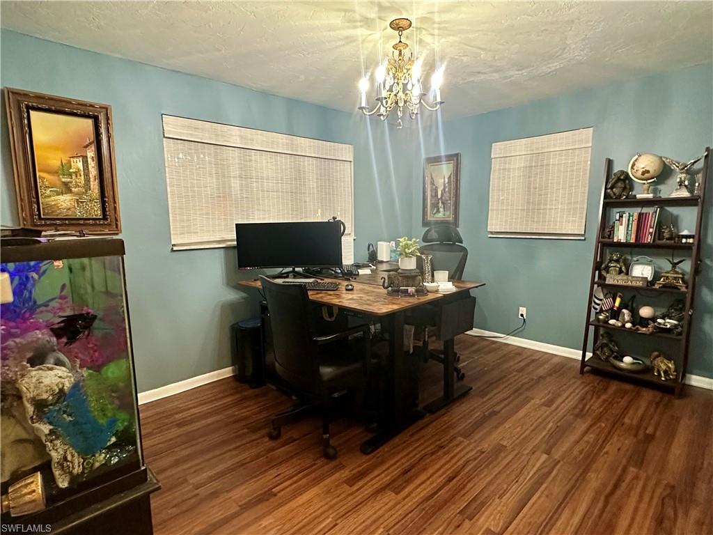 Interior room featuring wood-finish flooring, two windows with woven blinds, and a central chandelier