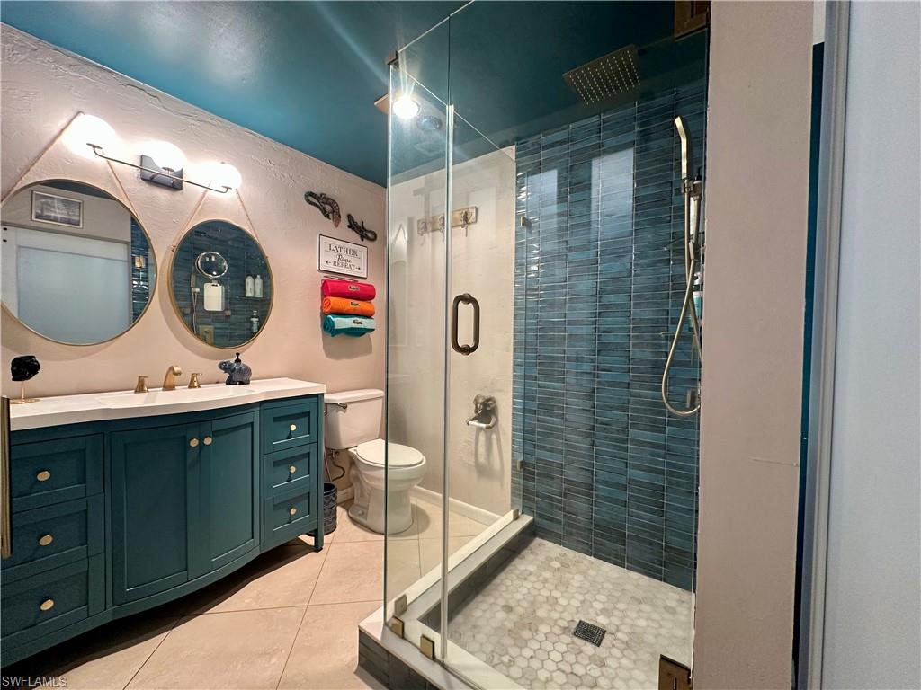 Bathroom featuring a glass-enclosed shower with blue subway tile, a rain showerhead, a teal vanity with a white countertop, and dual circular mirrors