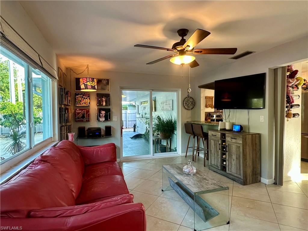 Tiled flooring throughout this space features a ceiling fan with integrated lighting, extensive windows, and sliding glass doors providing access to the exterior