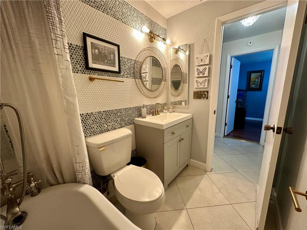 Bathroom featuring a patterned tile accent wall, a freestanding clawfoot tub with an attached shower, and a single vanity with storage