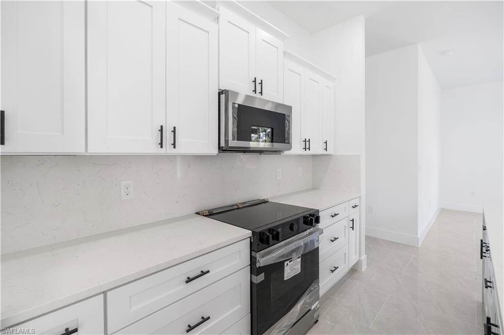 Contemporary kitchen featuring white shaker cabinetry with matte black hardware, stone countertops with a matching backsplash, a stainless steel over-the-range microwave, and a black range