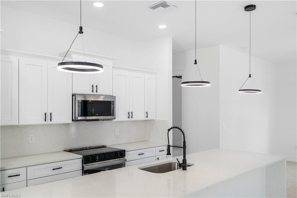 Kitchen featuring white shaker-style cabinetry with black hardware, stainless steel microwave, black range, and light-toned countertops