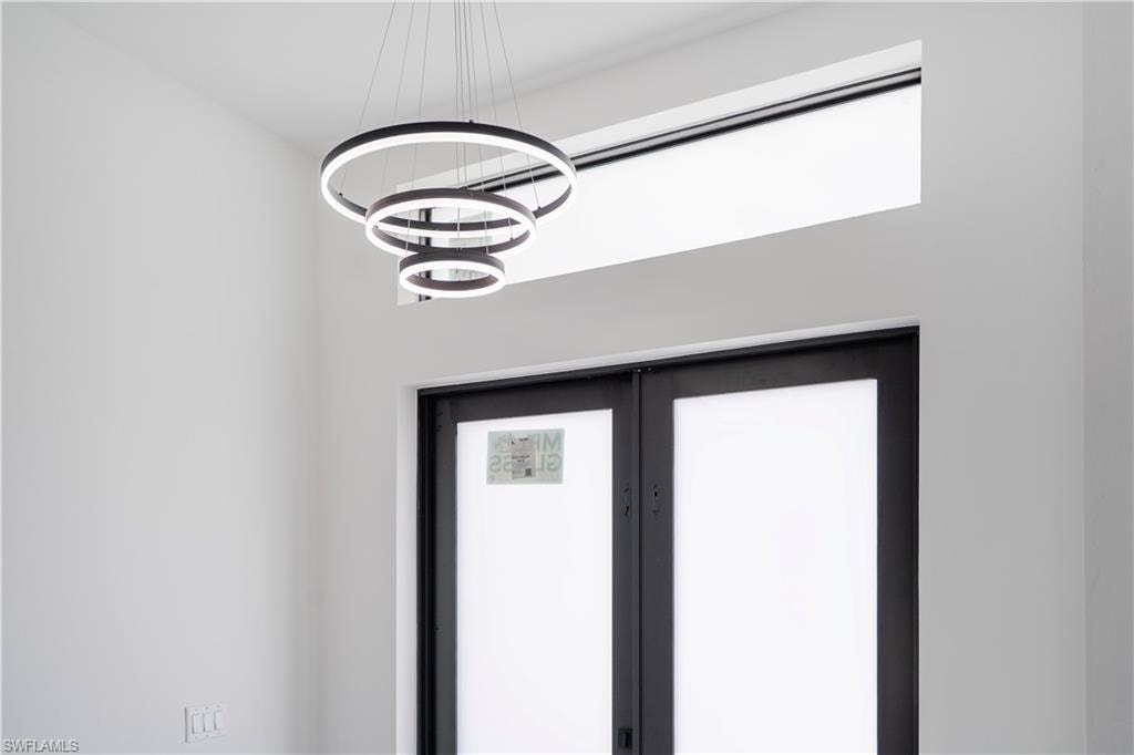 Modern tiered ring chandelier illuminating a white interior with a transom window and a dark-framed double door