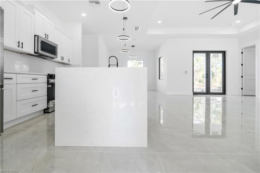 Modern kitchen featuring a large center island with a black gooseneck faucet, white shaker cabinetry with black hardware, stainless steel appliances, and a matching white backsplash