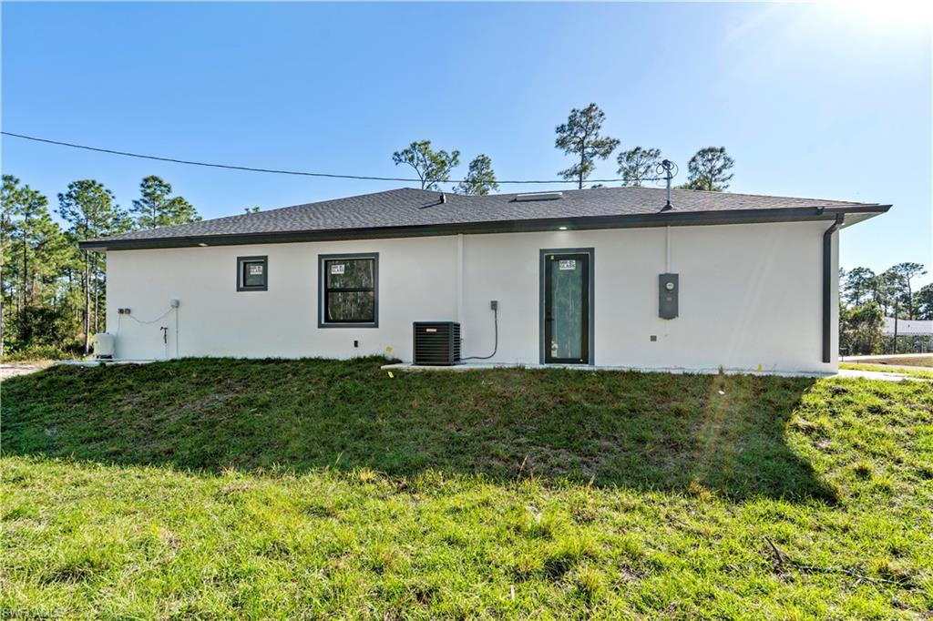 Contemporary stucco exterior featuring a dark asphalt shingle roof, dark-framed windows, and a black-framed rear entry door