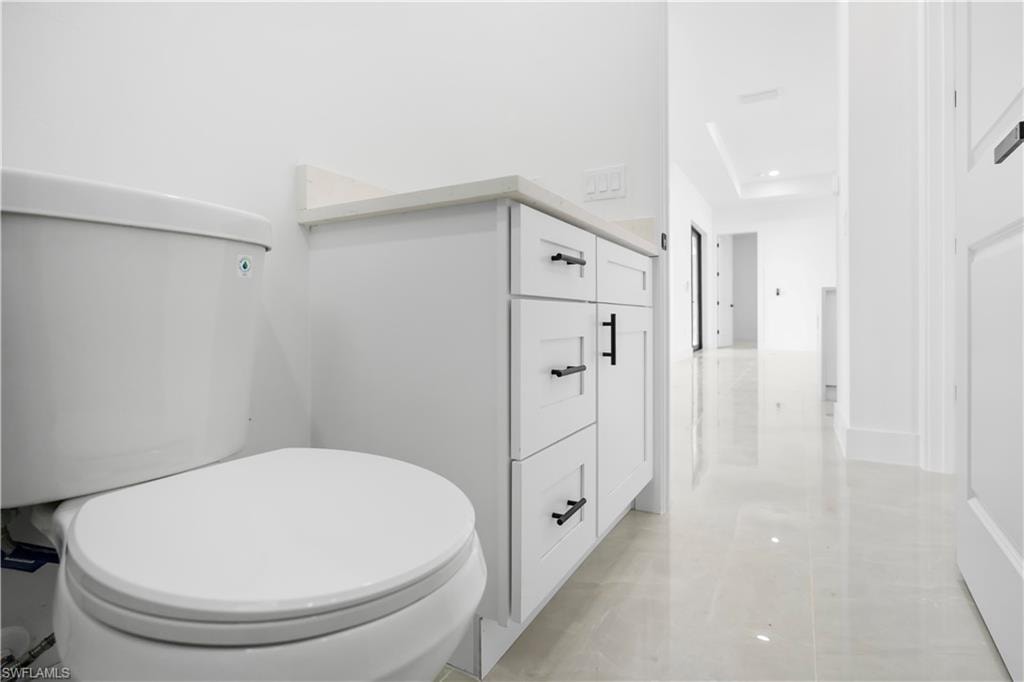 White shaker vanity with quartz countertop and matte black hardware, complementing the polished tile flooring and white walls