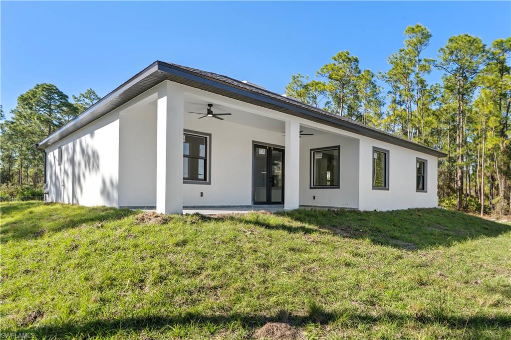 Rear exterior featuring a covered patio with an outdoor ceiling fan, white stucco finish, and dark-framed windows
