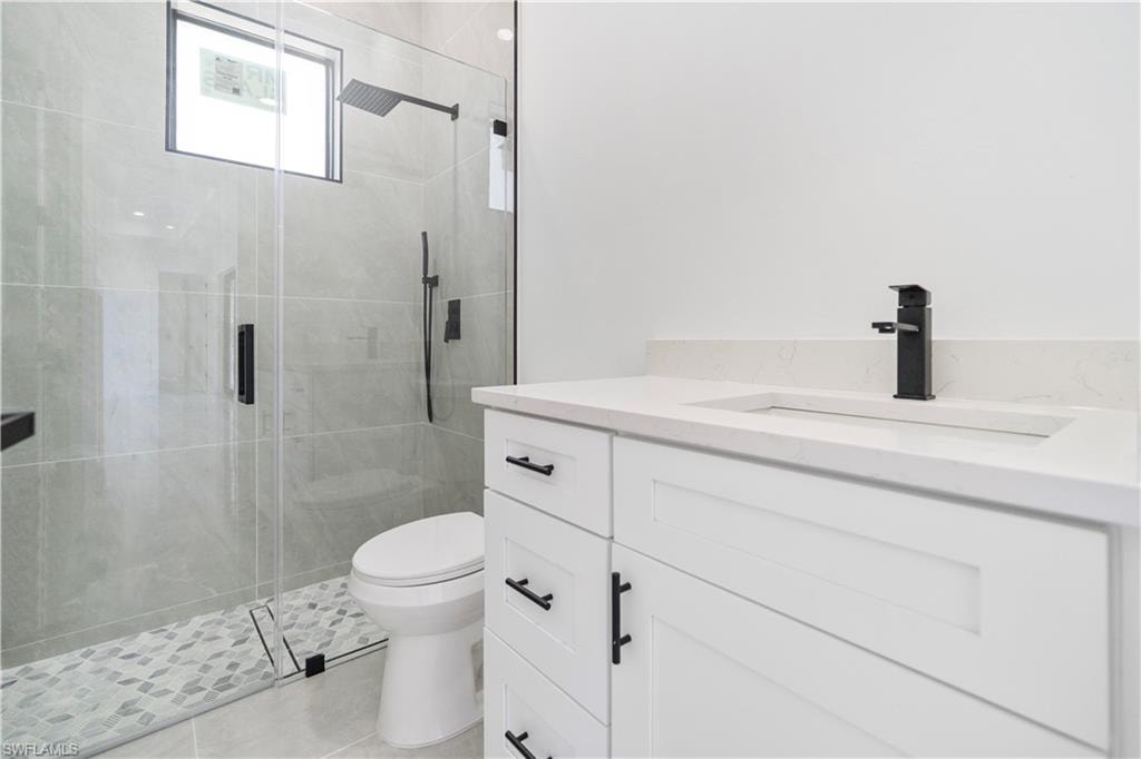 Contemporary bathroom featuring a frameless glass shower enclosure, a rain shower head, a built-in shower niche, a white vanity with shaker-style cabinetry, and a countertop with an integrated sink