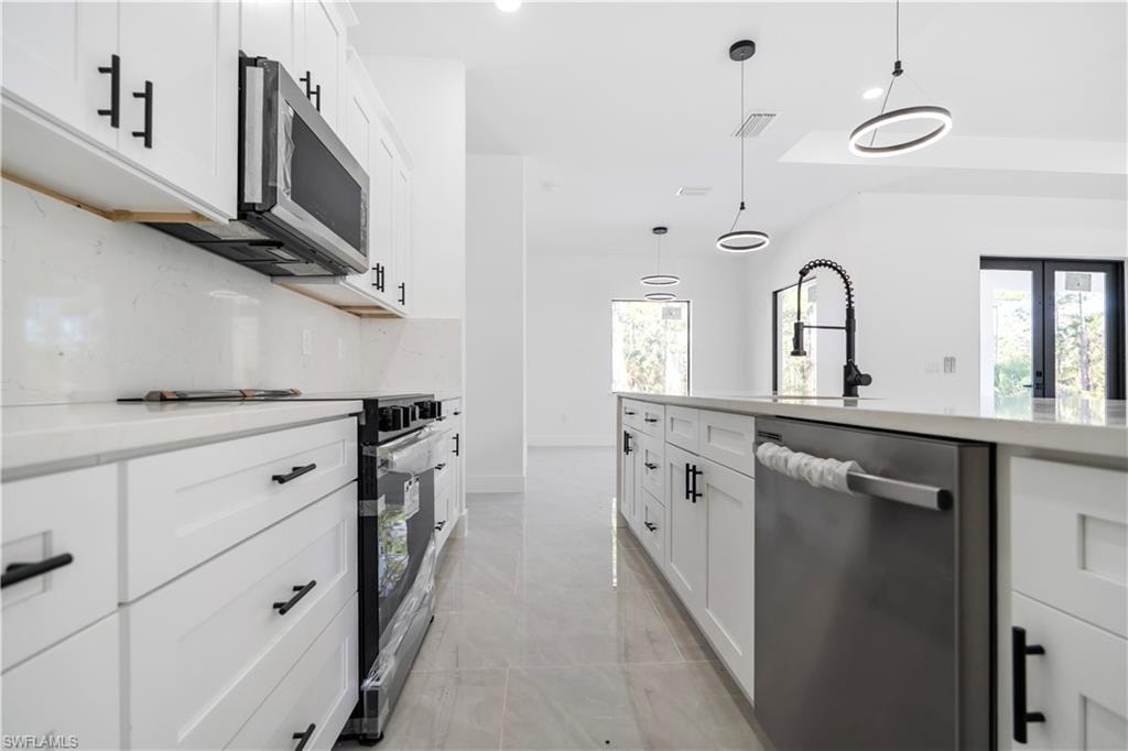 Modern kitchen featuring white shaker cabinetry, stainless steel appliances, a center island with a large sink, and contemporary pendant lighting