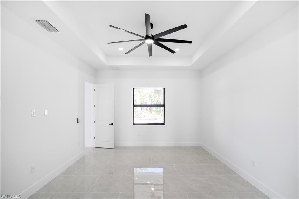 Room featuring large format tile flooring, a tray ceiling, recessed lighting, a ceiling fan, and a single window with dark trim