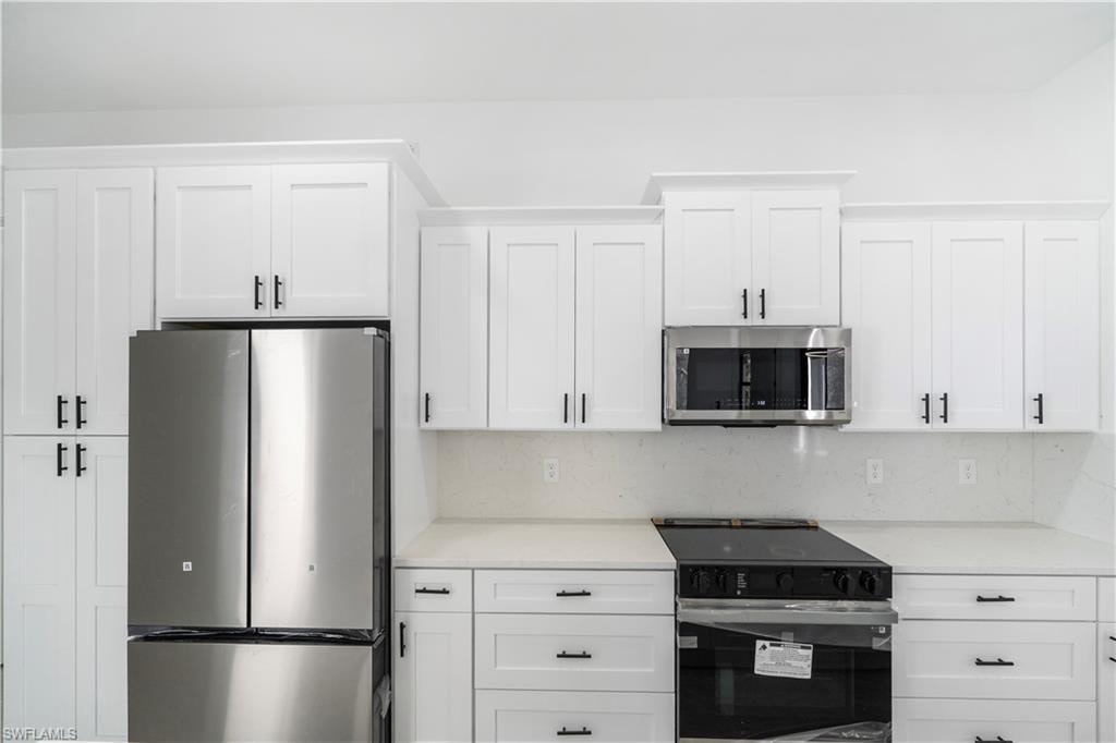 Kitchen featuring white shaker-style cabinetry with matte black hardware, stainless steel appliances, a built-in microwave, and light-toned countertops