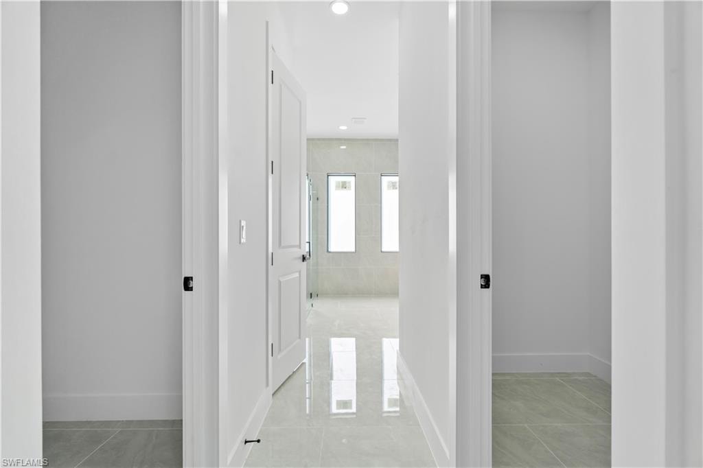 Hallway featuring light gray tile flooring, crisp white walls, recessed ceiling lighting, and a white paneled door with matte black hardware