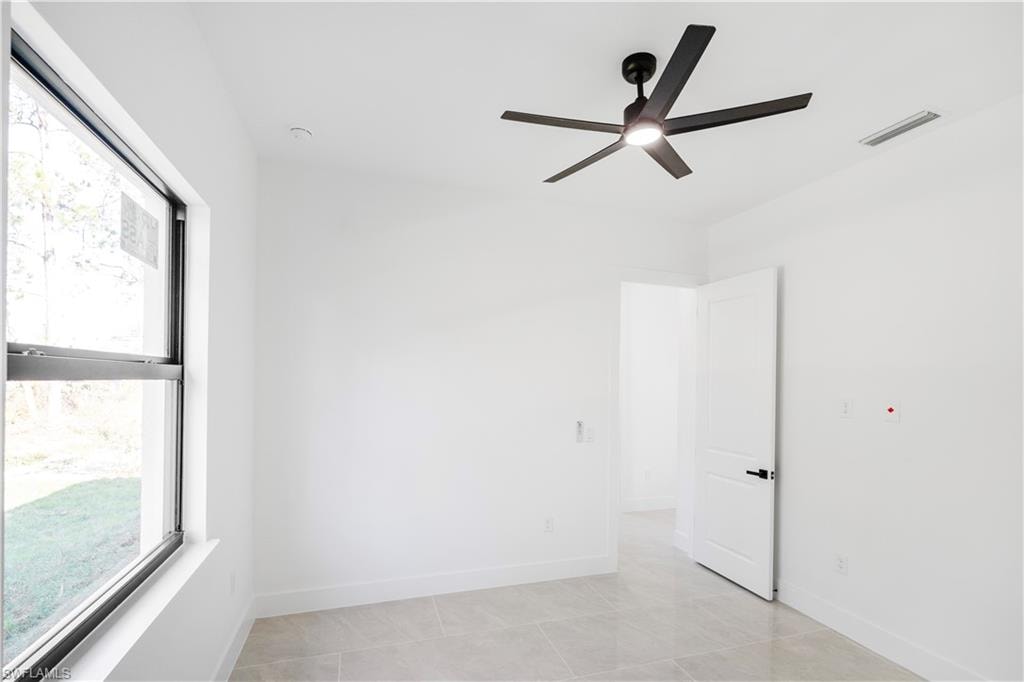 Room with a ceiling fan featuring integrated lighting, large window, white walls, and light-toned tile flooring