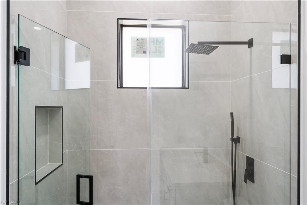 Frameless glass shower enclosure featuring a matte black rainfall showerhead, matching handheld shower, and a built-in shower niche