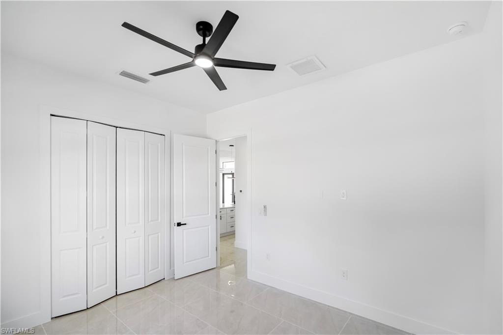 Bright interior space featuring a contemporary ceiling fan with integrated lighting, bi-fold closet doors, a paneled door with matte black hardware, white baseboards, and light-toned tile flooring