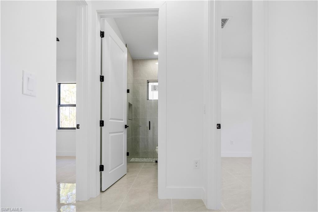Hallway with light-toned tile flooring throughout, white walls, and white interior doors with black hardware