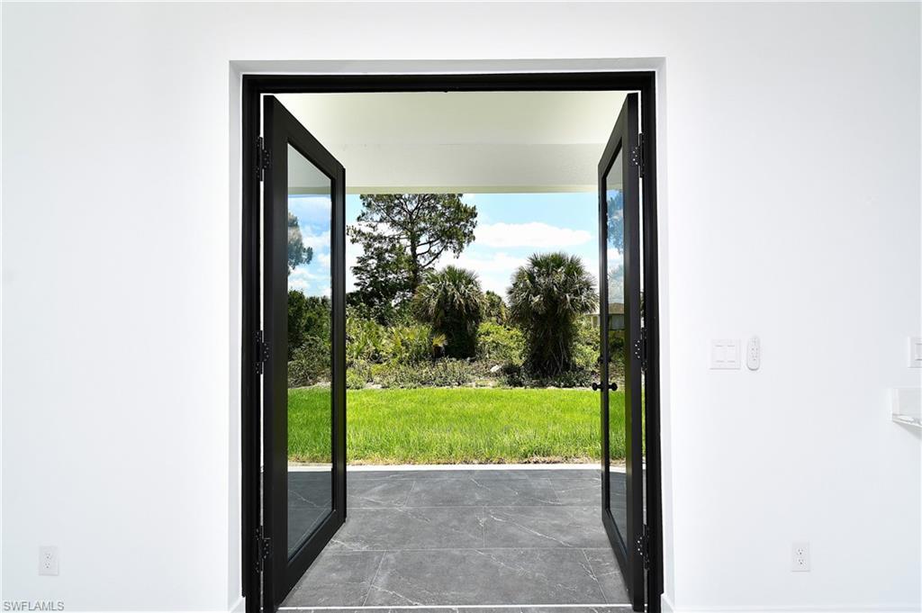 Black-framed glass French doors opening to an outdoor patio with dark tile flooring