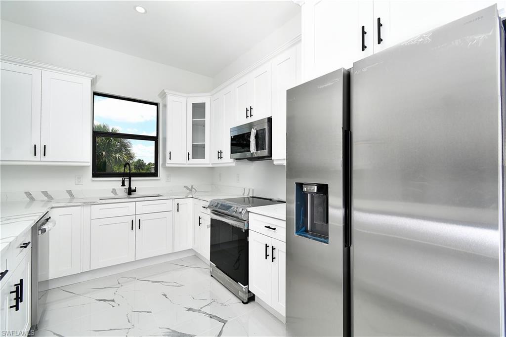Modern kitchen featuring white cabinetry, stainless steel appliances, a black sink with a matching faucet, marbled flooring, and recessed lighting