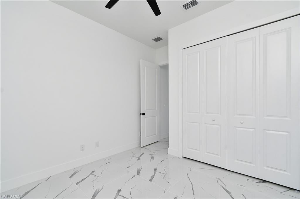 Room featuring large format tile flooring with distinctive veining, a ceiling fan with black blades, and a white bi-fold closet system