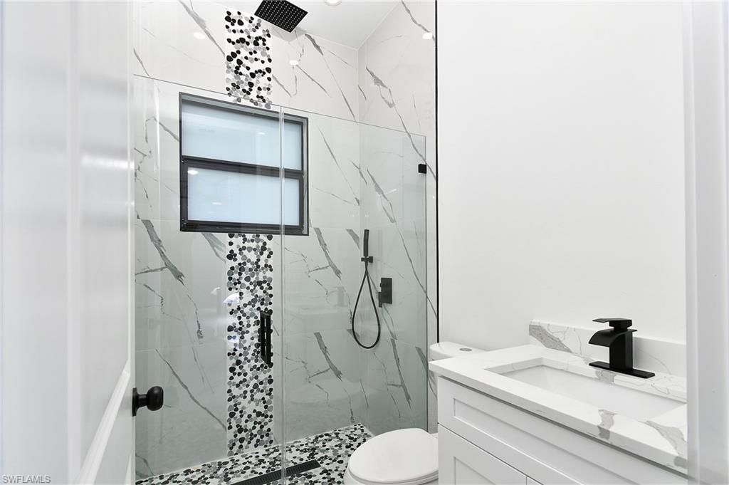 Glass-enclosed shower with a rainfall showerhead, large format marble-look tile, decorative mosaic tile accents, and a window