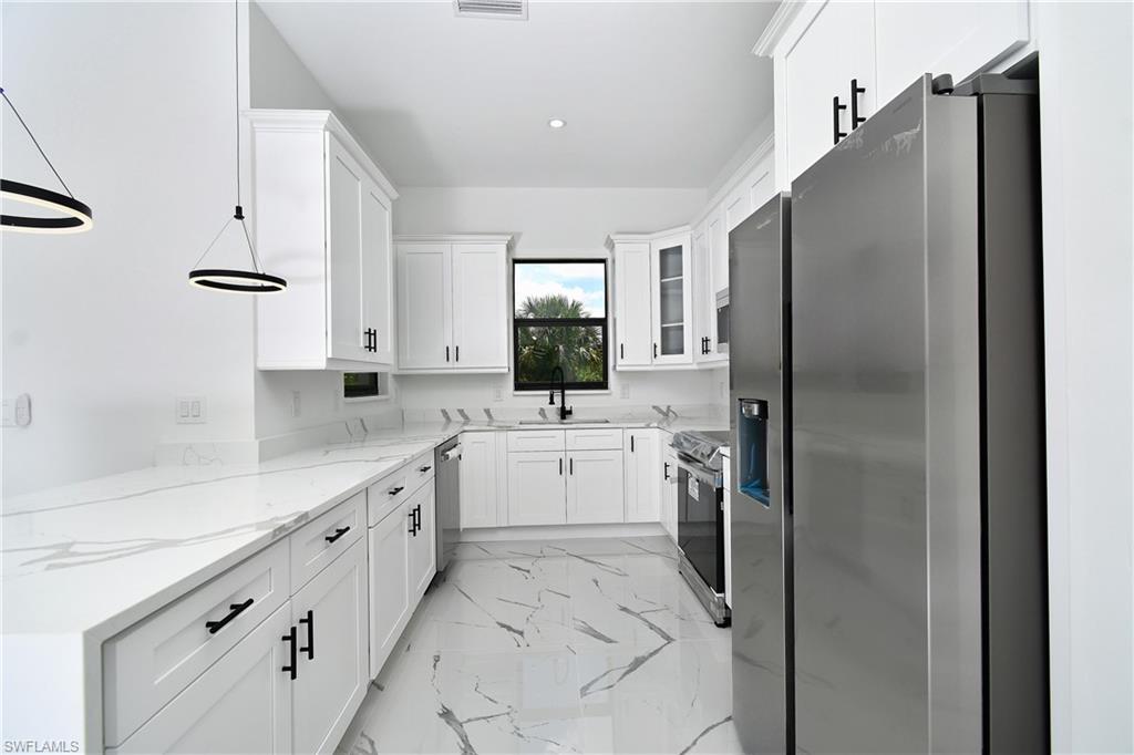 Contemporary kitchen featuring white cabinetry with black hardware, white countertops, stainless steel appliances, and large format floor tiles