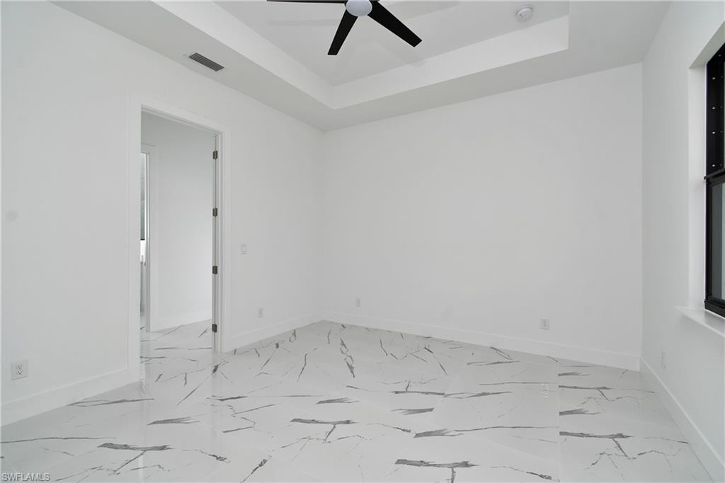 Spacious room featuring white walls, a tray ceiling with a black ceiling fan, and large format marble-look tile flooring