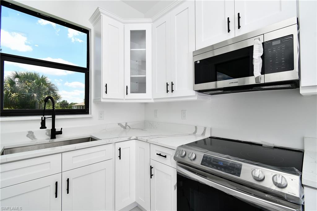 Kitchen featuring white shaker-style cabinetry, white countertops with gray veining, a stainless steel undermount sink with a matte black faucet, and a stainless steel over-the-range microwave