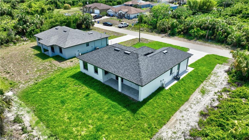 Modern white exterior with dark shingle roof, covered patio, concrete driveway, and a partially grassed lot