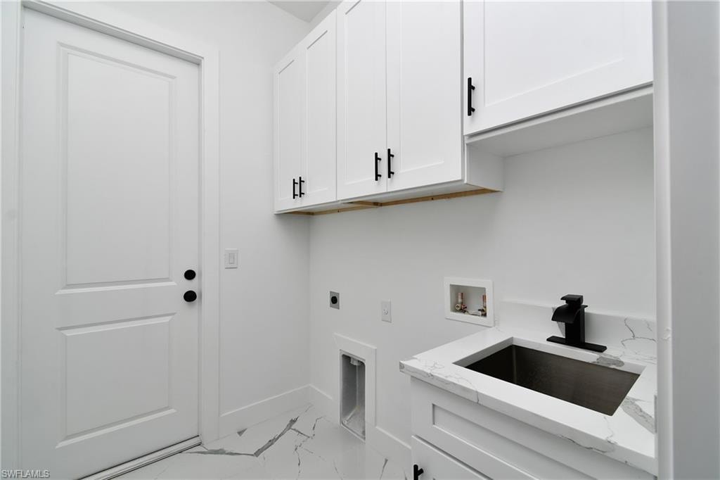 Dedicated utility space featuring white shaker-style cabinetry with matte black hardware, a stainless steel sink with a matte black faucet, and a countertop with subtle veining